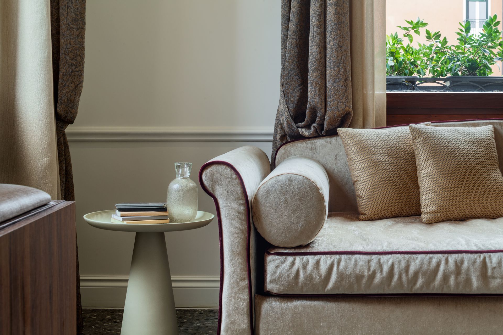 Cozy living room corner with a cream sofa, side table, and window with curtains and pillows.