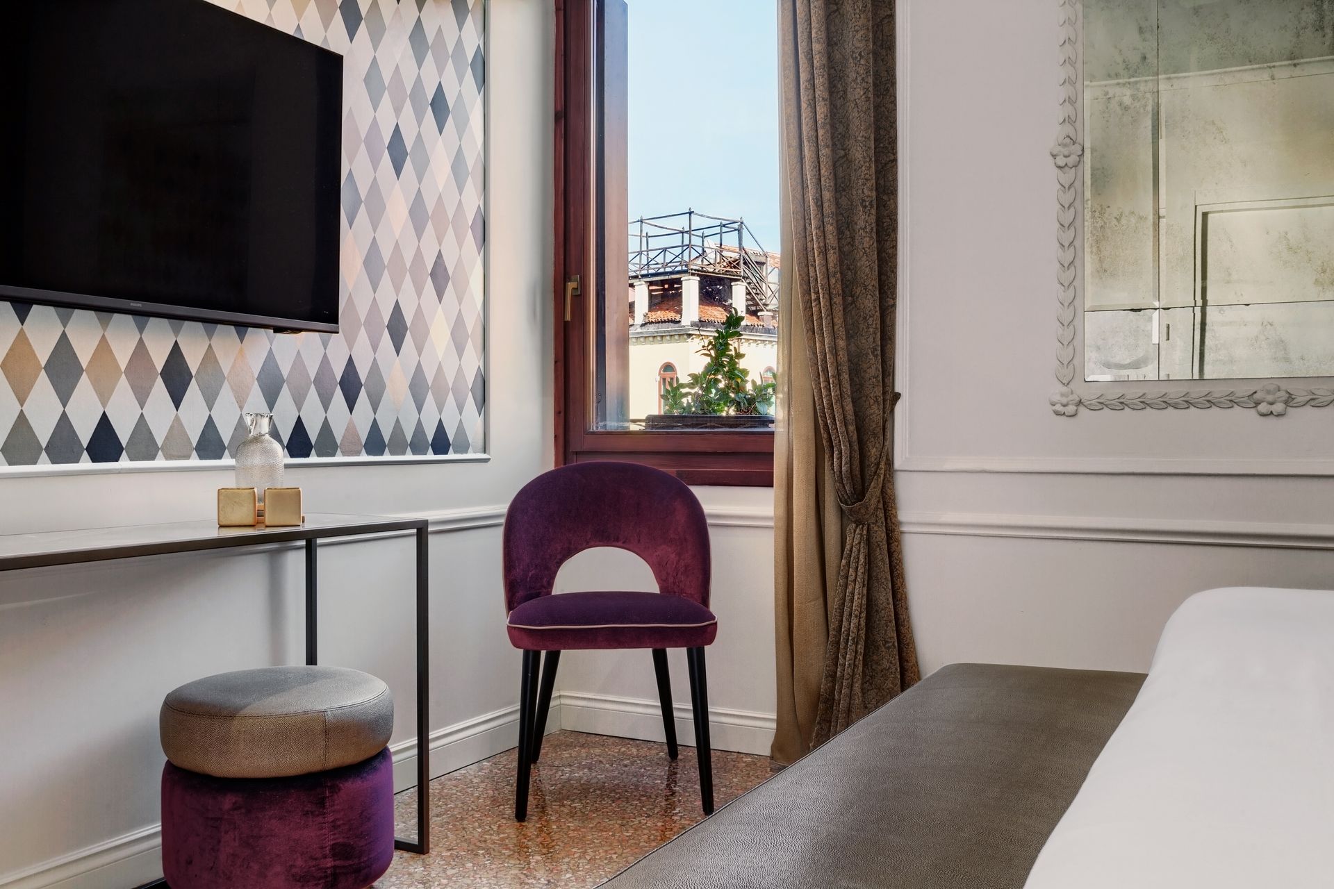 Hotel room with purple chair by a window, desk, and bed in a softly lit interior