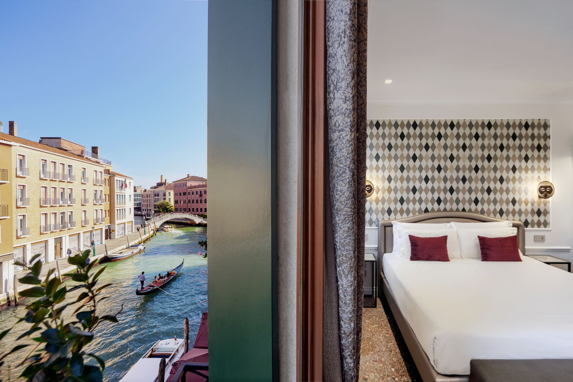 Hotel room with bed overlooking a canal and pastel buildings through a floor-to-ceiling window