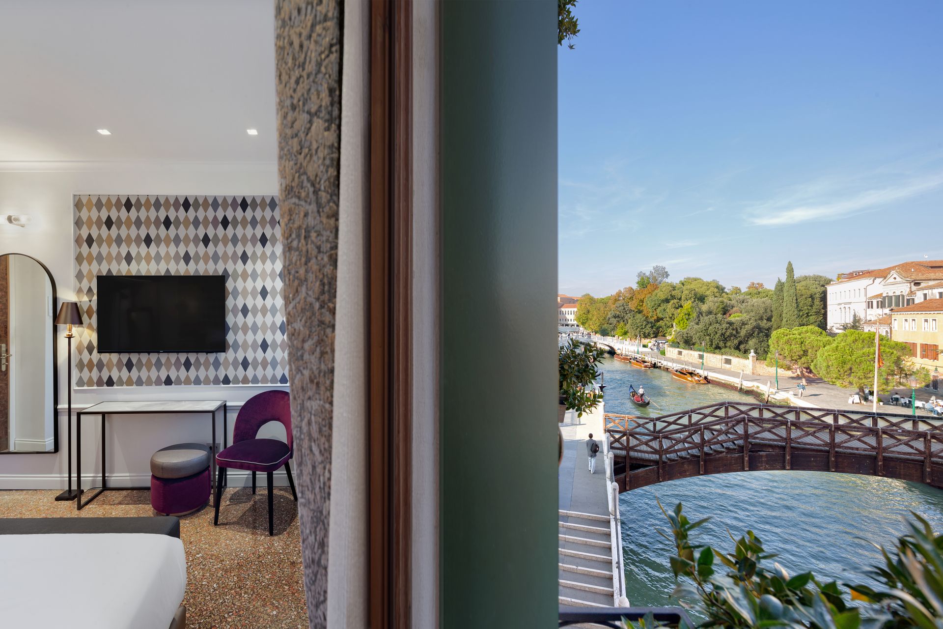 Modern hotel room with canal view, patterned tile wall, purple chair, and a bridge outside the window