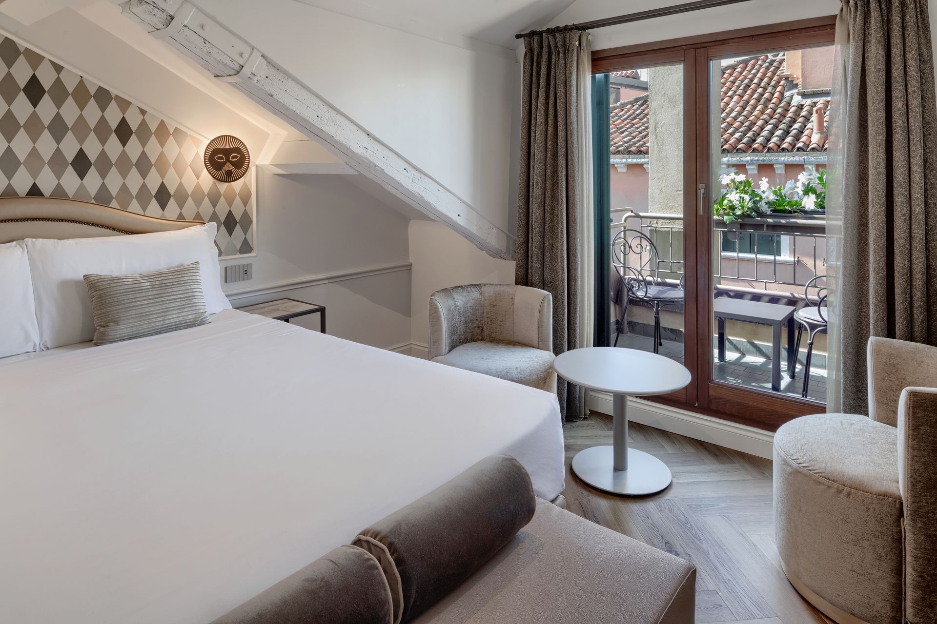 Cozy bedroom with a bed, armchair, small table, and balcony doors letting in daylight