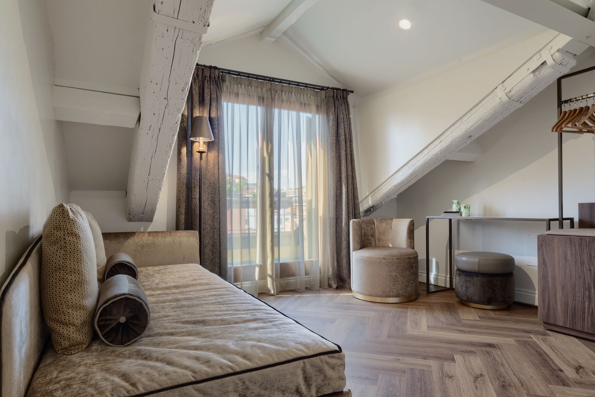 Cozy attic bedroom with sofa bed, armchair, desk, and sheer curtains by a skylight window