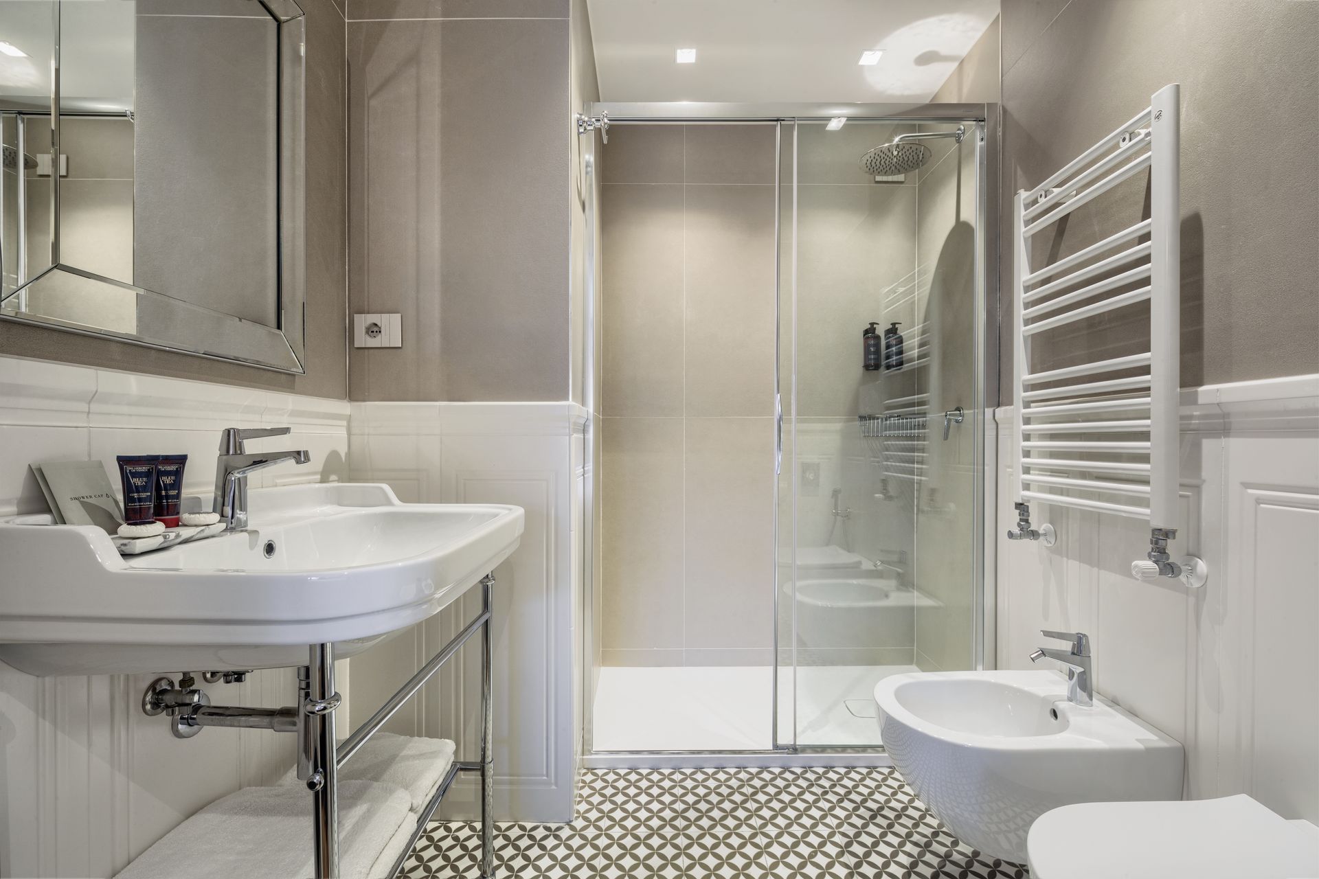 Modern white bathroom with sink, toilet, shower, towel radiator, and patterned floor tiles