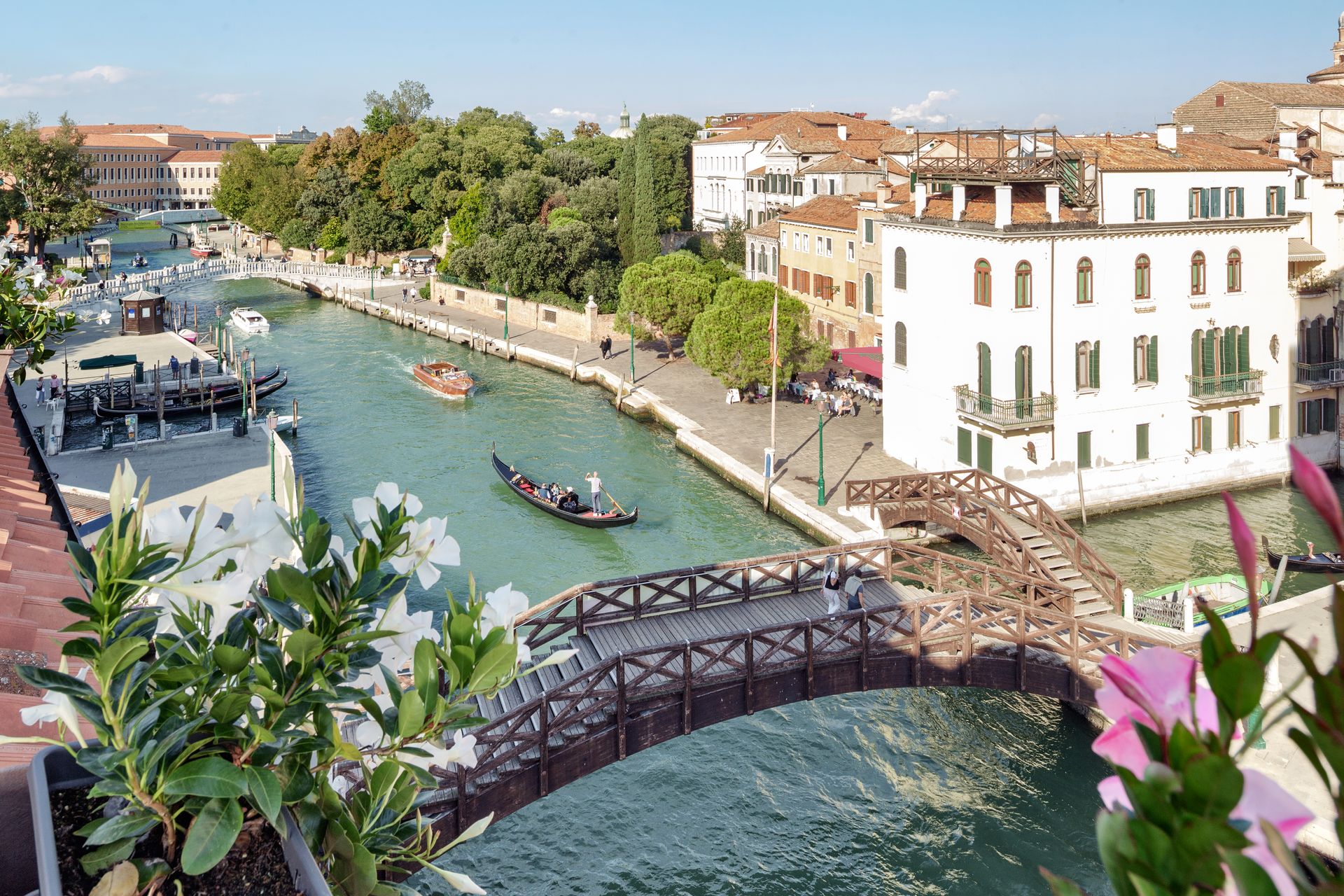 Canal in Venice with boats, arched bridge, and white waterfront buildings on a sunny day