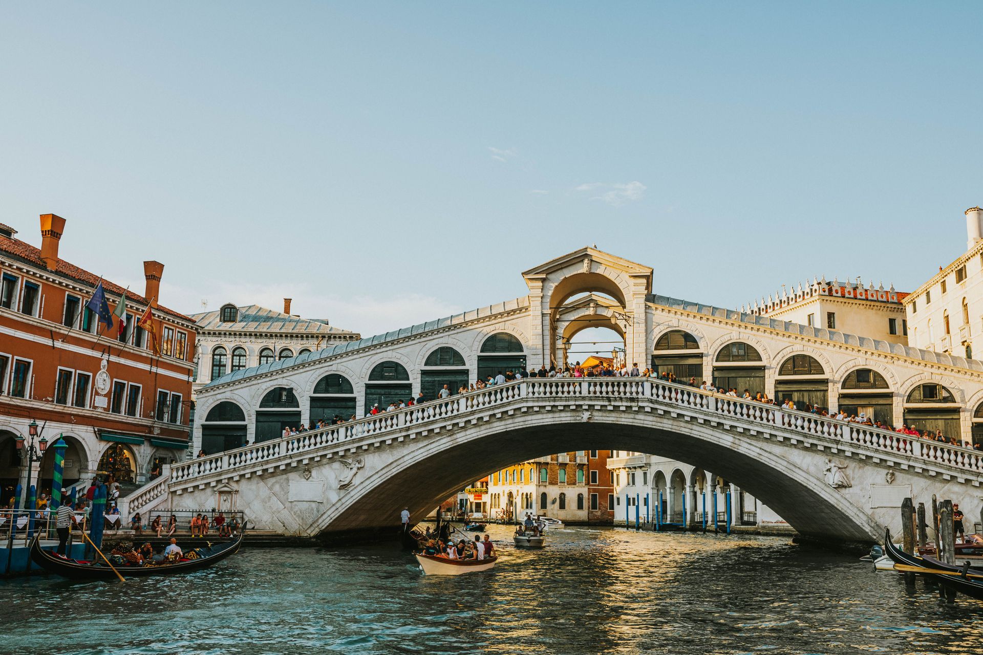 Il Ponte di Rialto a Venezia si staglia sopra un canale, accanto a colorati edifici storici, sotto un cielo sereno