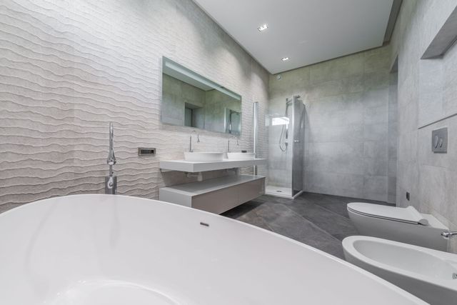 Bagno moderno bianco con vasca freestanding, doppio lavabo, cabina doccia e pavimento in piastrelle grigie.