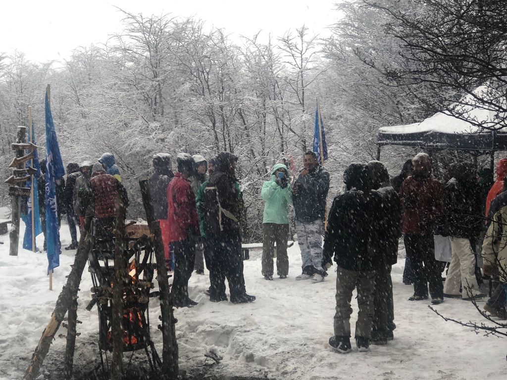 La gente se reunió al aire libre, en bosques nevados, alrededor de un fuego, con banderas y tiendas de campaña visibles.