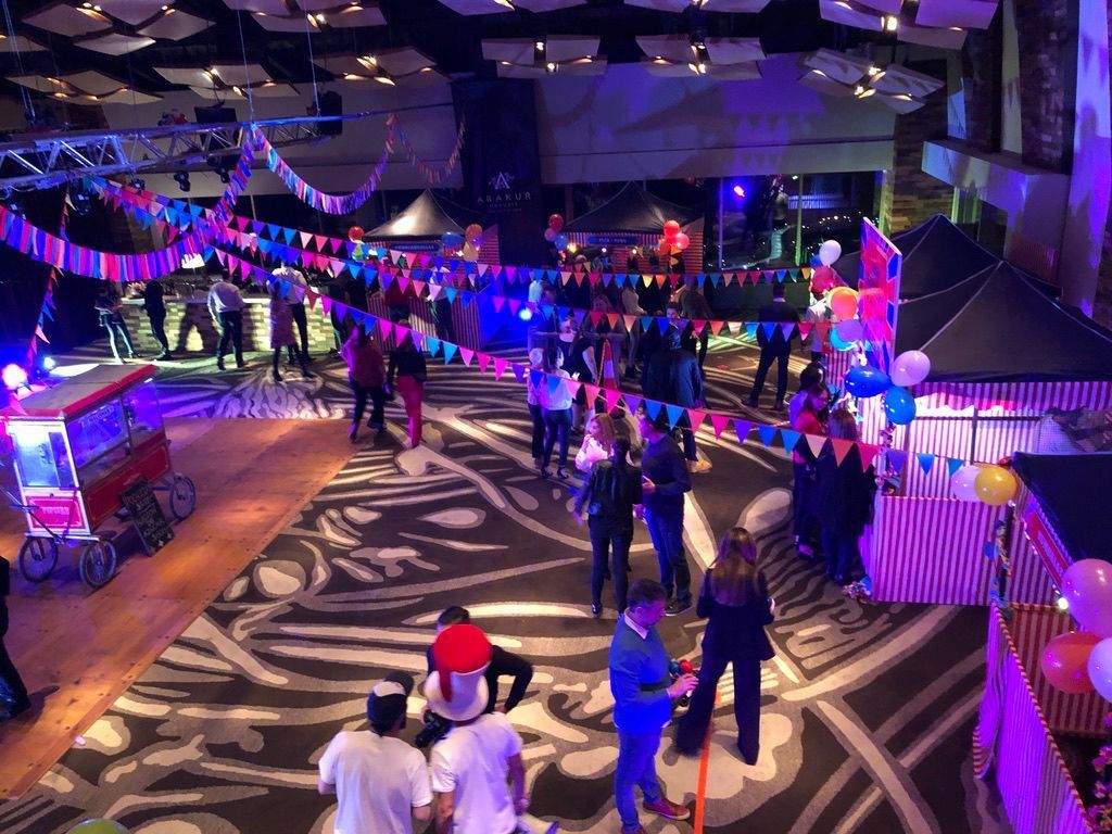 Gente en una colorida fiesta con temática de circo en un gran salón con decoraciones y stands.