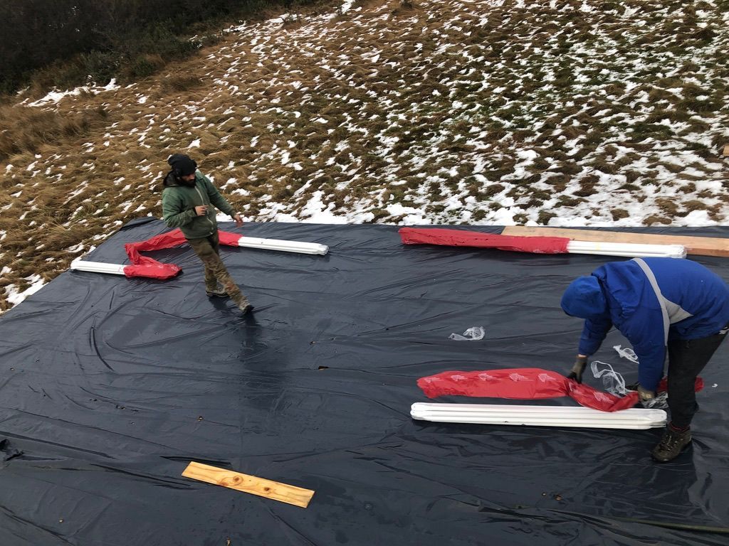 Dos personas desenrollan barreras rojas y blancas sobre una lona negra, con una ladera nevada de fondo.