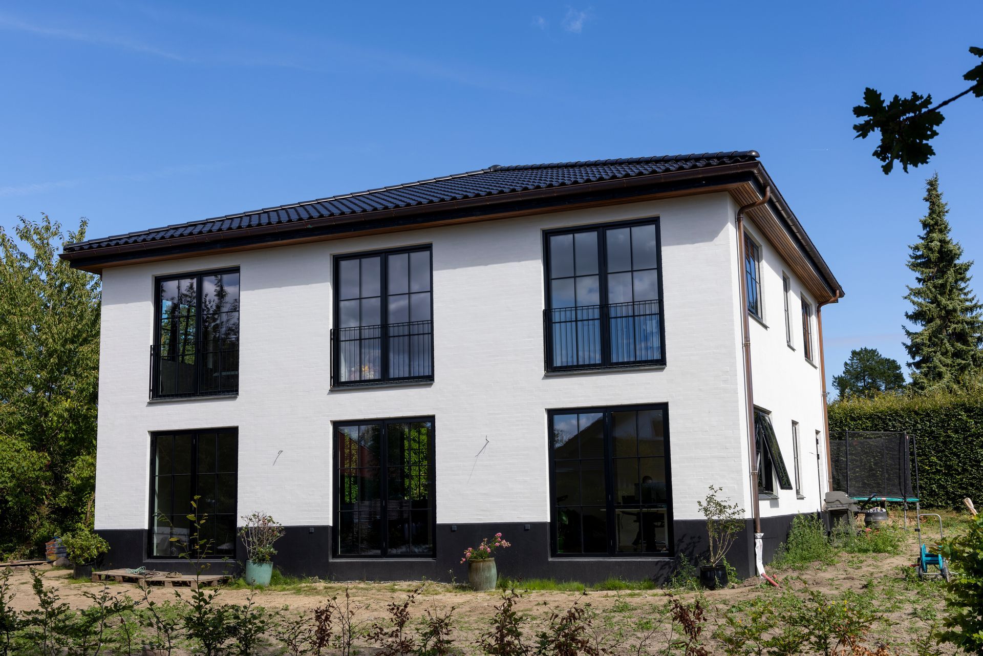 Moderne hvidt toetagers hus med mørkt tag og store vinduer i en solrig have