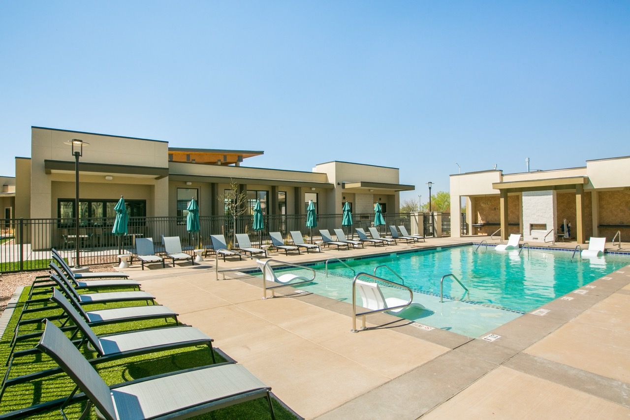 Outdoor apartment pool with lounge chairs, teal umbrellas, and sunlit surroundings.