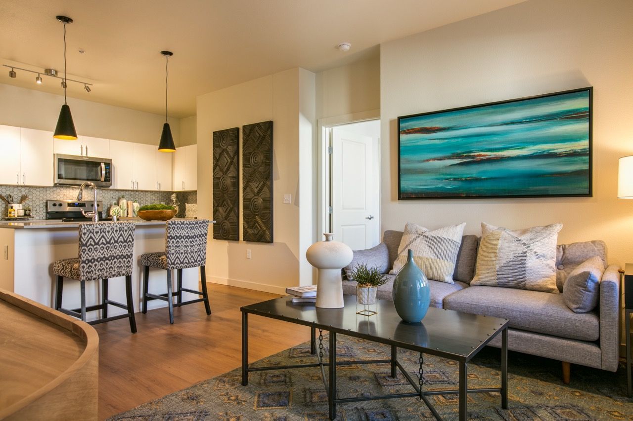 Open-concept living area with kitchen island, two patterned bar stools, and a gray sofa.