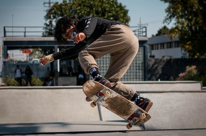 Person skateboarding in a skate park, performing a trick. They wear black long sleeve, khaki pants, and patterned socks.