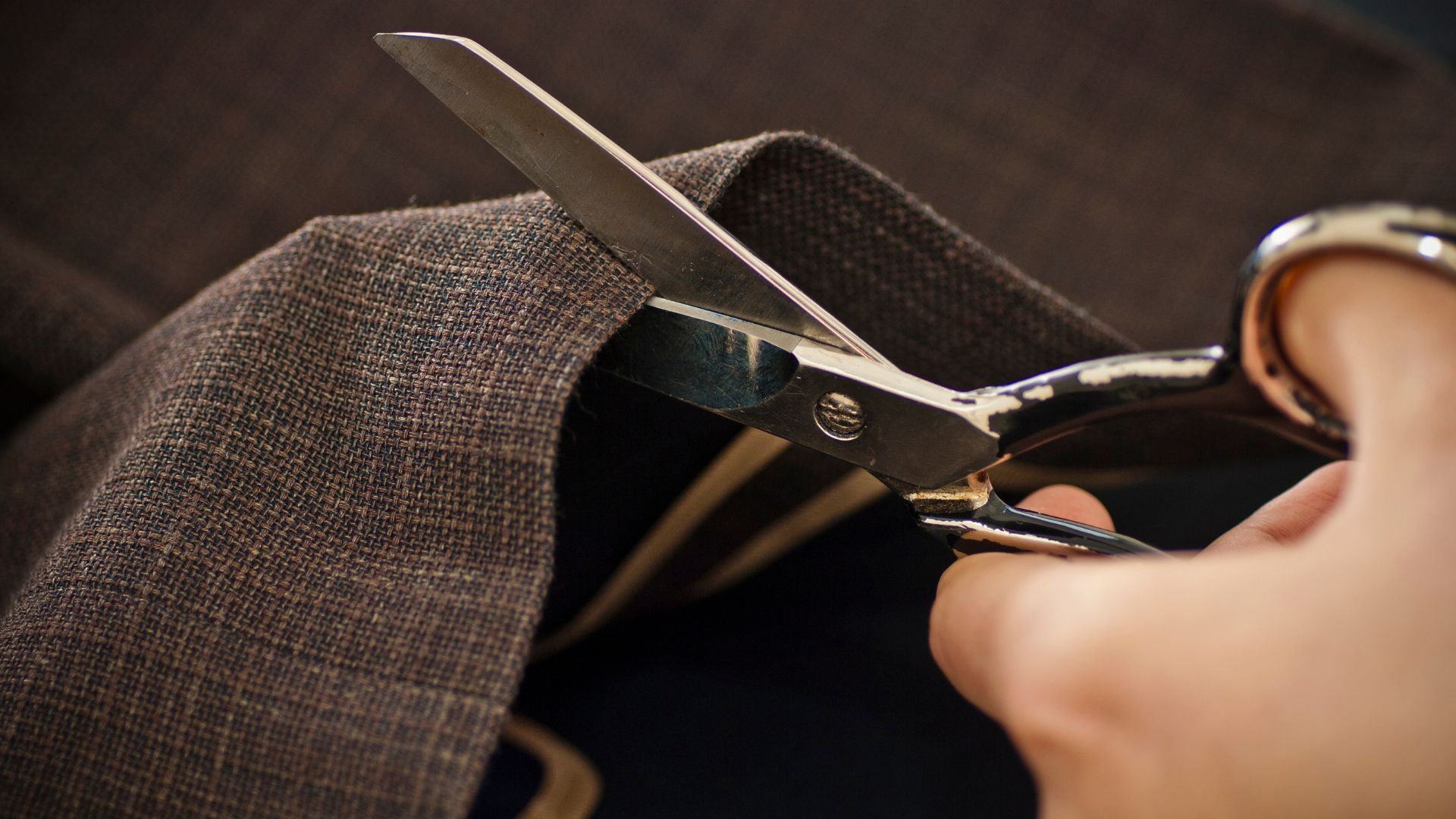Scissors cutting brown fabric close-up