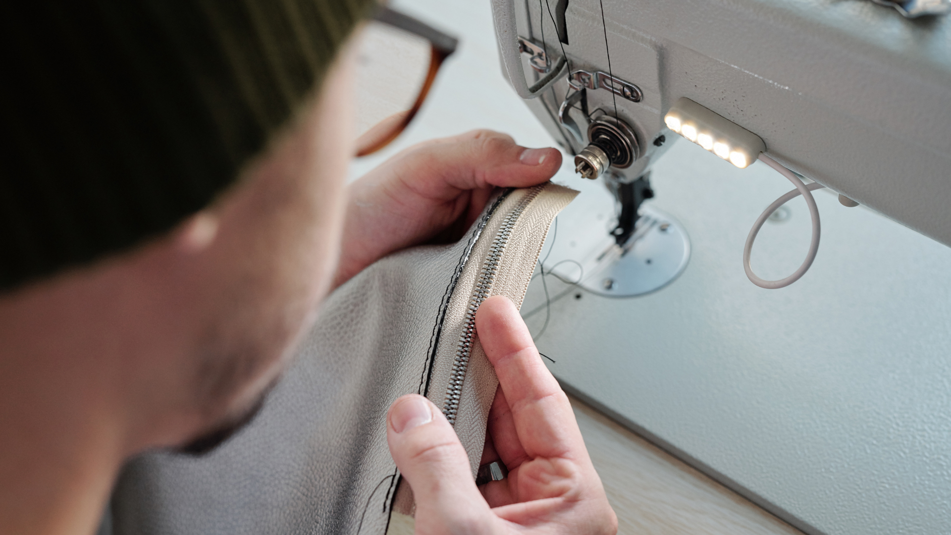 Hands sewing light gray fabric on a sewing machine close-up