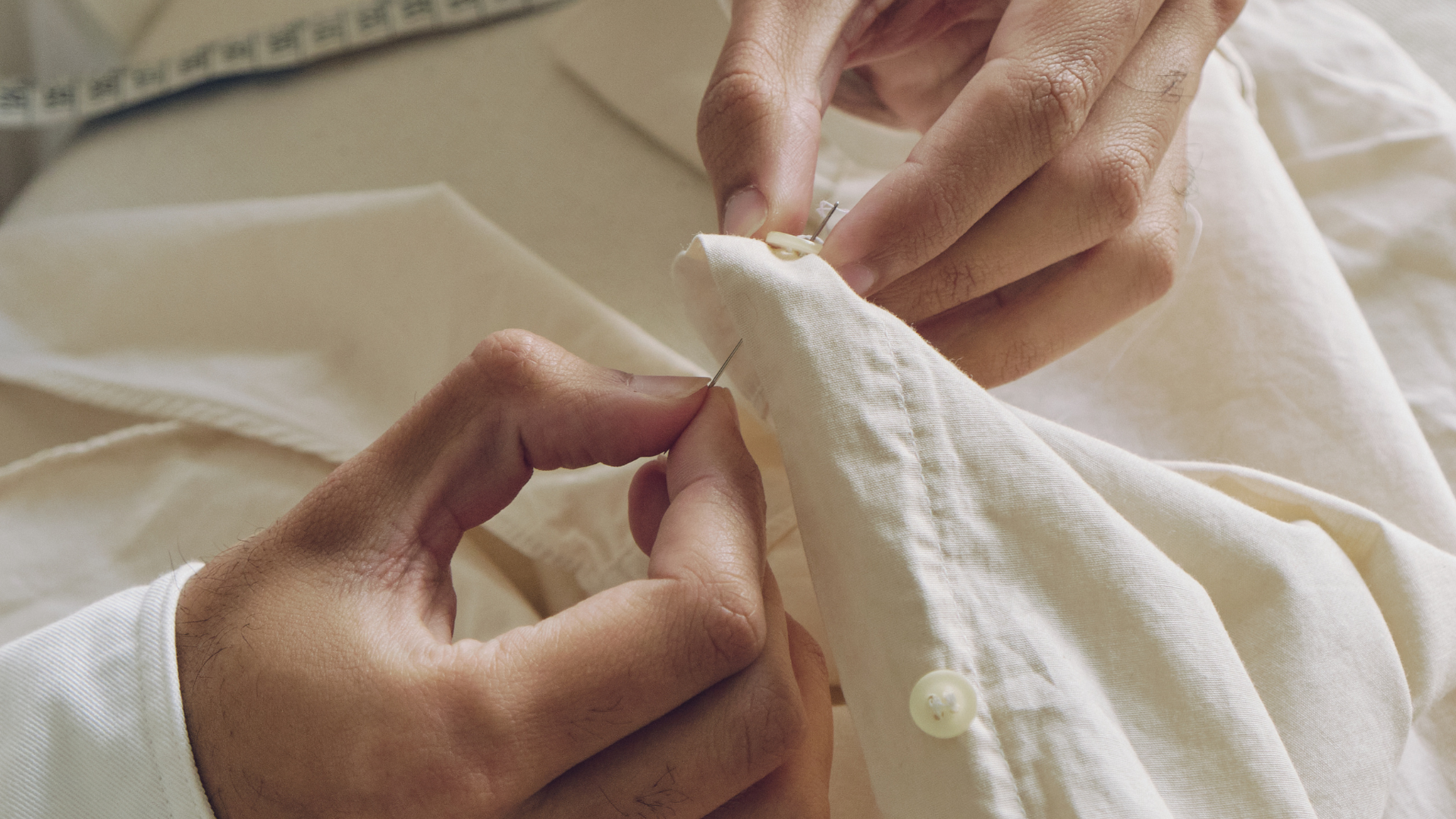 Hands sewing white fabric with a needle and thread
