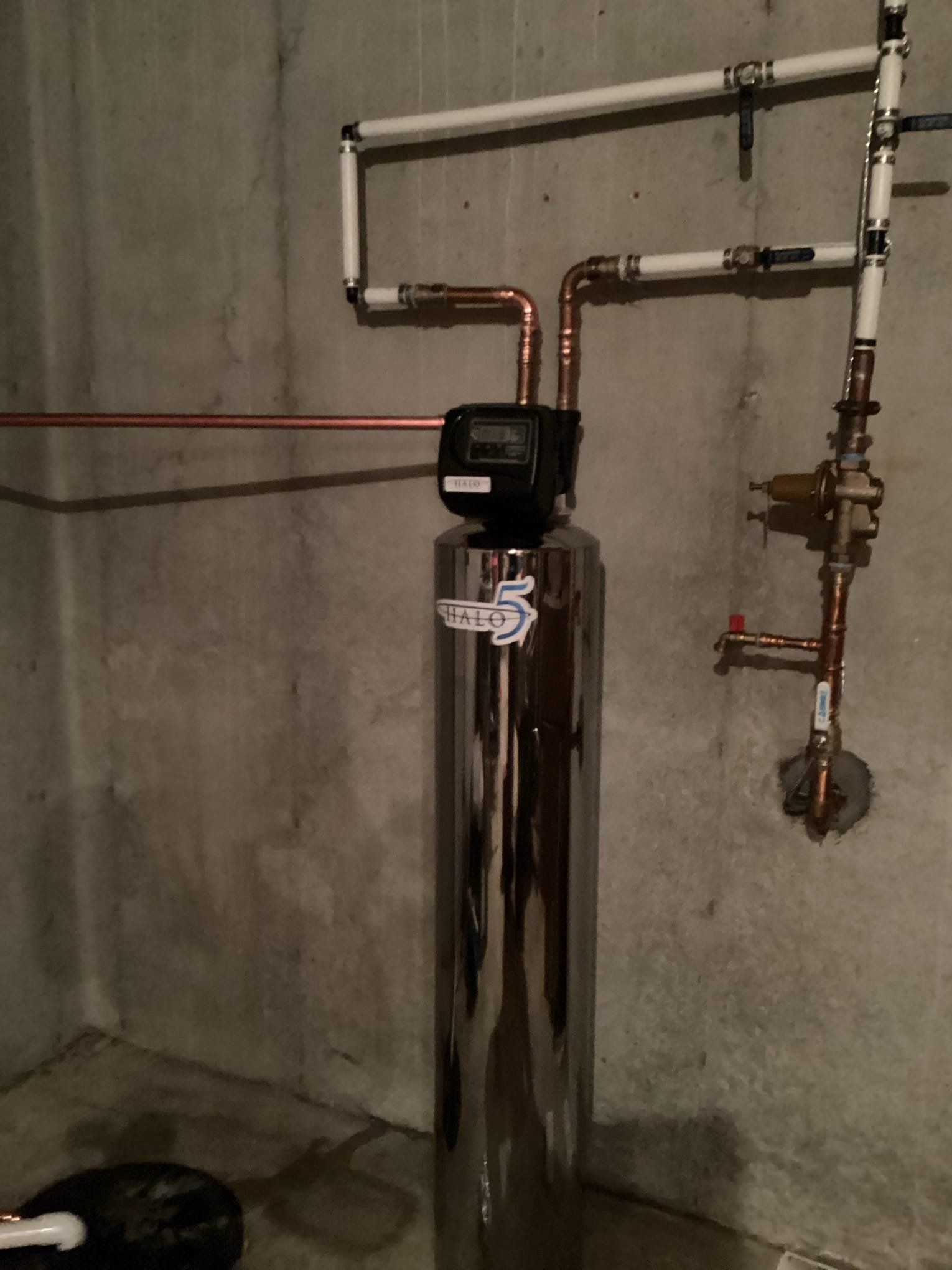Water softener tank with plumbing pipes in a basement utility area.