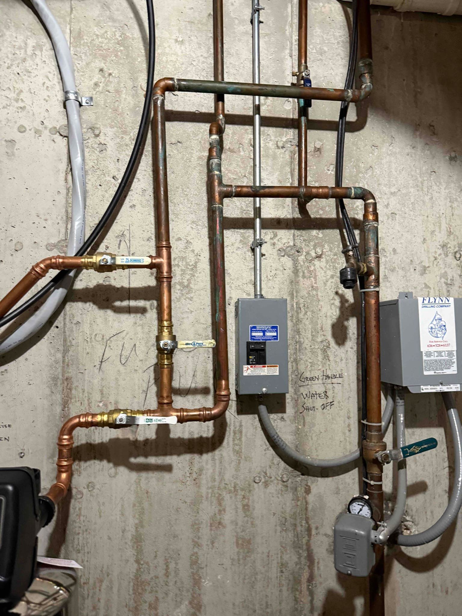 Copper pipes, electrical box, and pump mounted on a concrete wall.