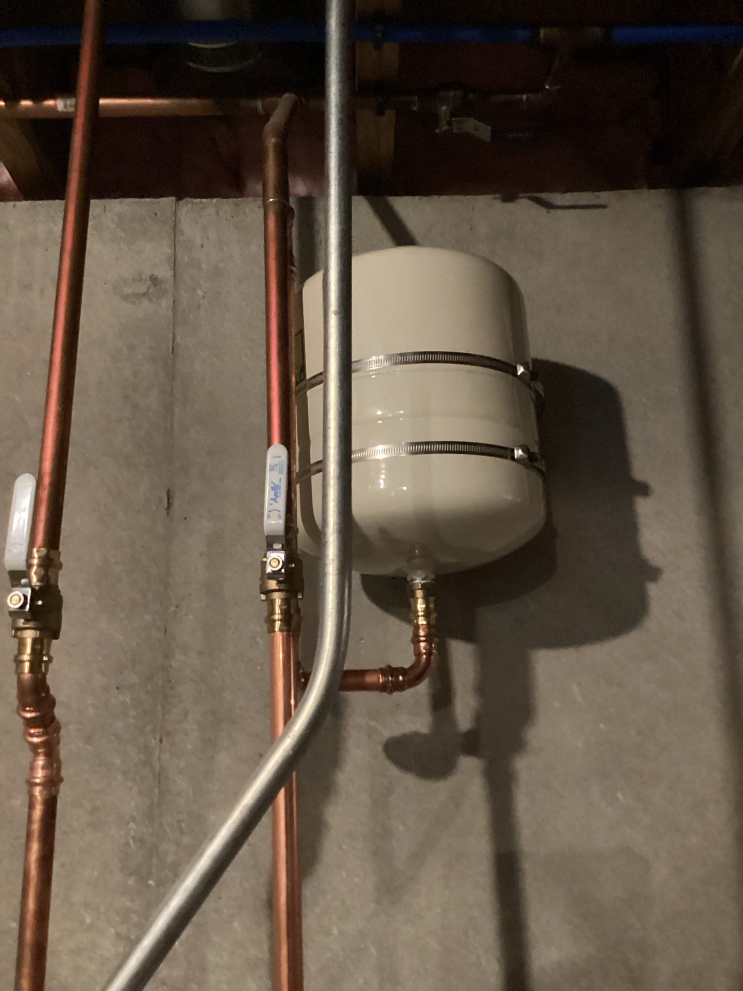 Basement wall with copper pipes and a white expansion tank on a gray concrete wall