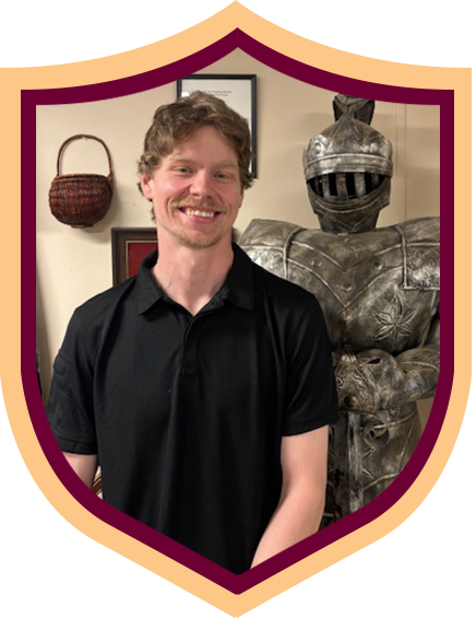 Smiling person in black polo standing beside a suit of armor in a framed portrait