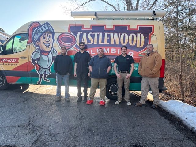 Five people standing beside a Castlewood Plumbing service van on a driveway in daylight