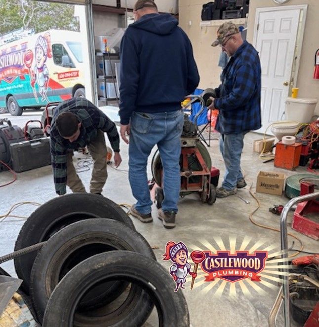 People working on a small engine in a cluttered garage, with tires and tools in the foreground.