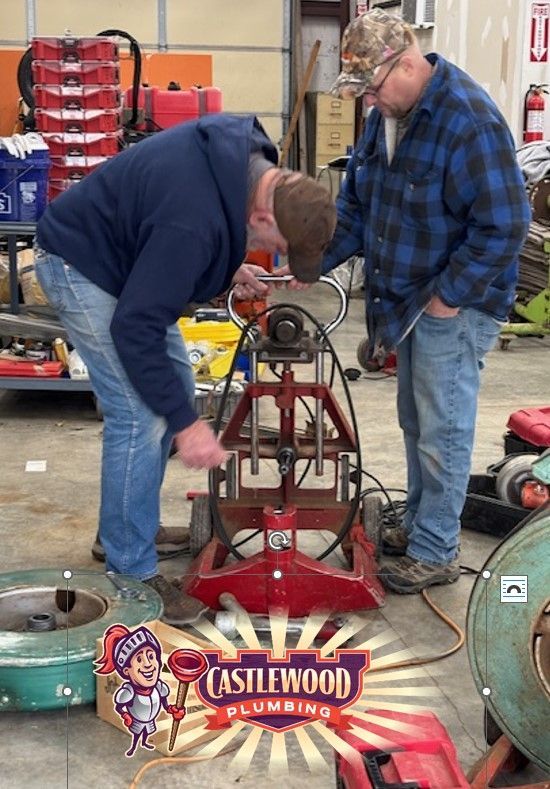 Two workers inspect a red machine in a workshop, with Castlewood Plumbing logo at the bottom.