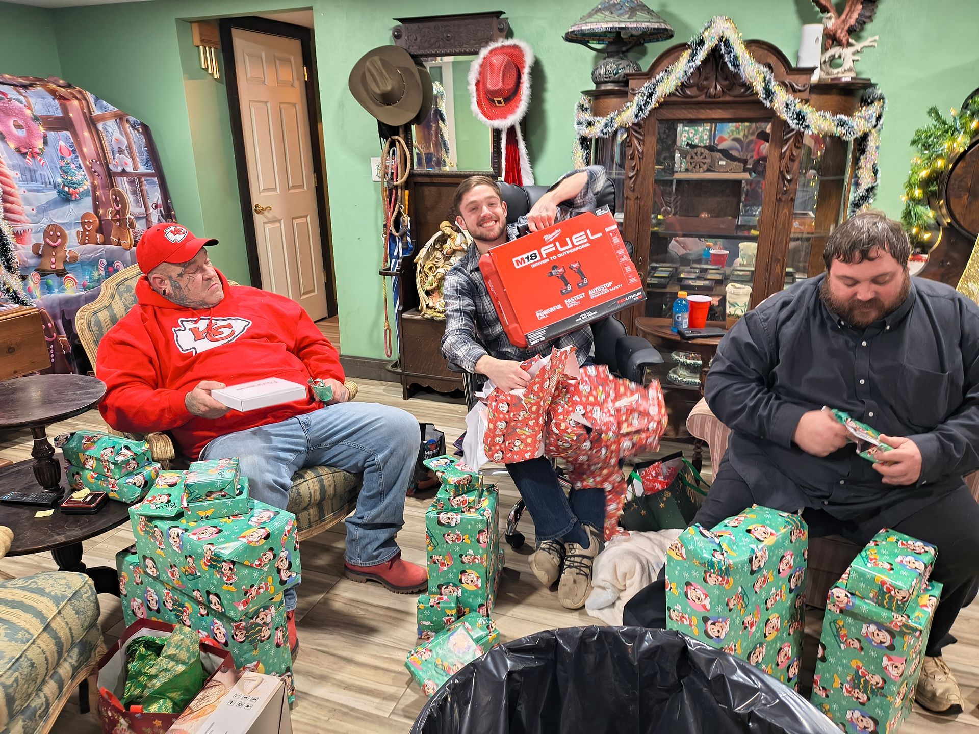 People opening gifts in a cozy room filled with Christmas decorations and wrapped presents.