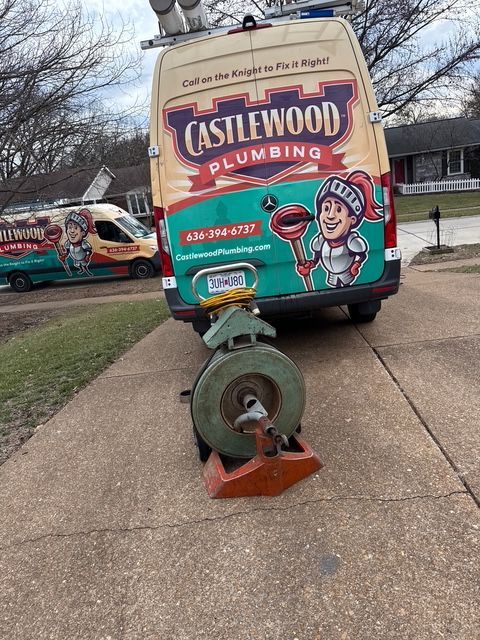 Castlewood Plumbing service van parked on a driveway beside a green grinder machine.