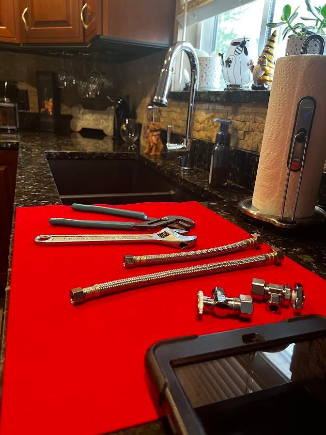 Plumbing tools and parts arranged on a red mat in a kitchen, near a faucet and sink.