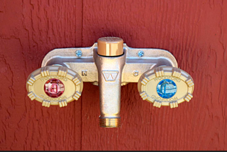 Brass water fixture with red and blue handles, mounted on a red wooden wall.