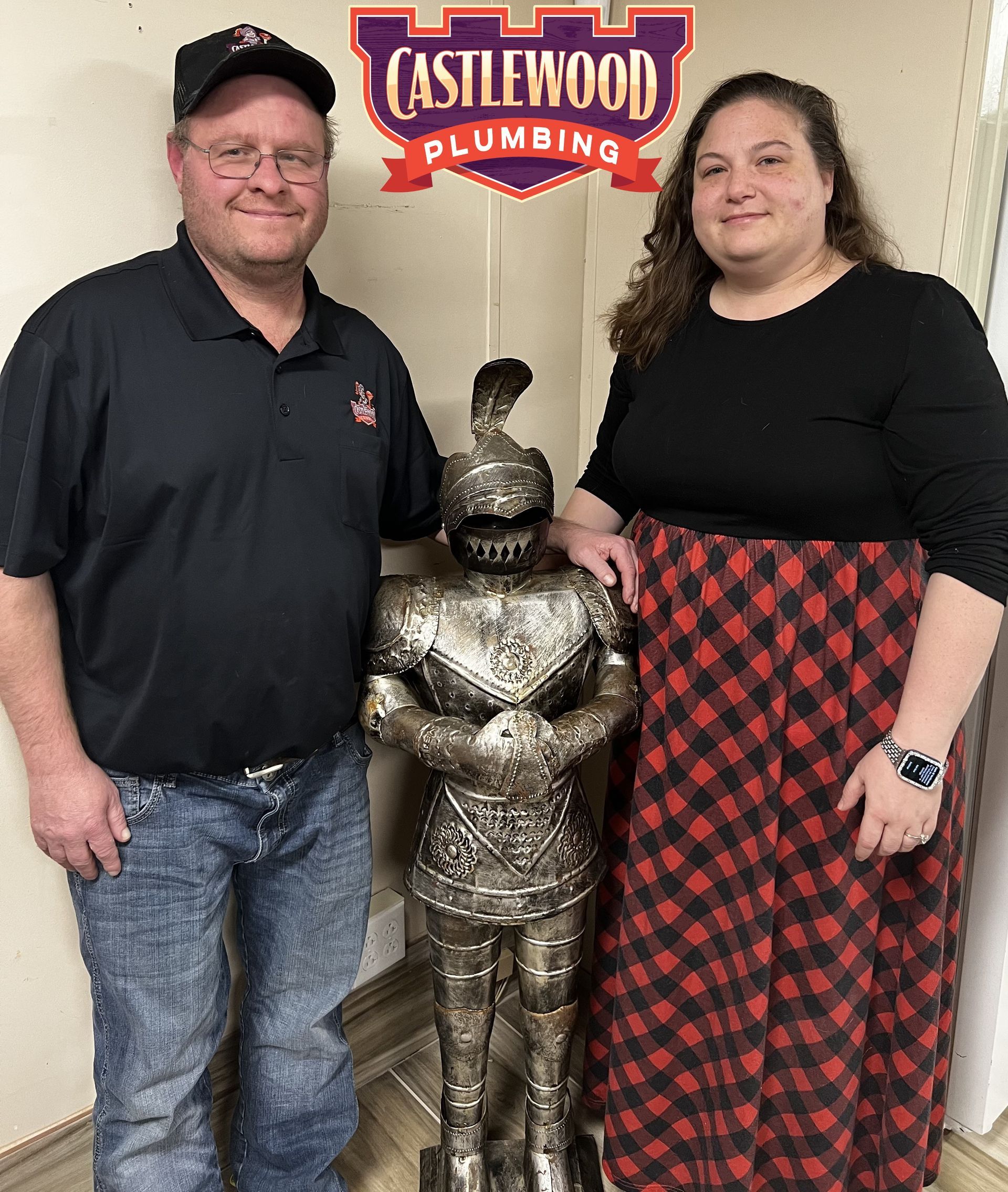 Two people stand with a metal knight statue in front of 
