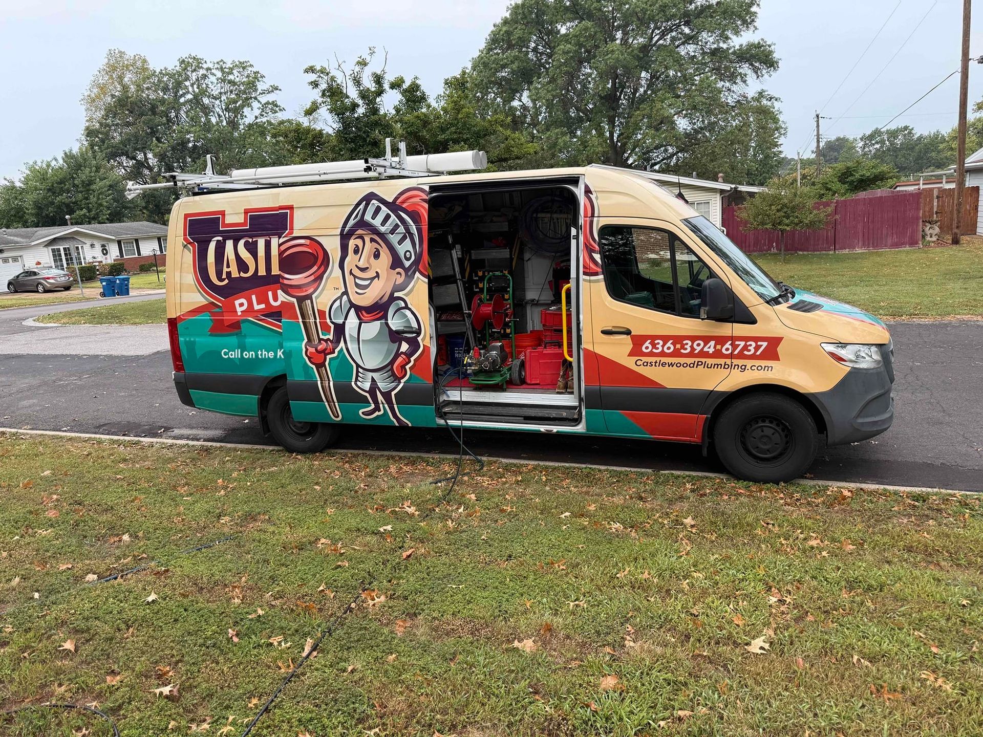 A Castle Plumbing van with open side door, colorful logo, parked on grassy area near residential homes.