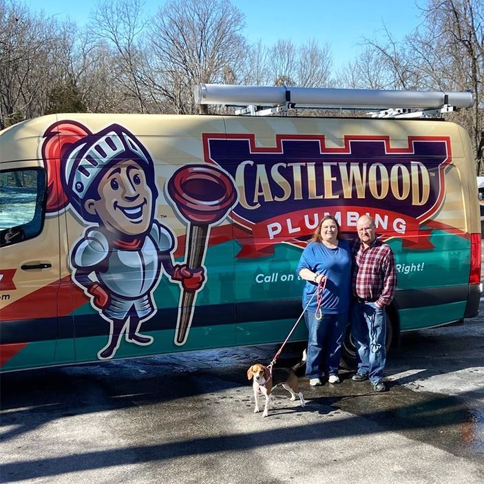 A couple and dog stand by a plumber van with knight logo, smiling outside on a sunny day.