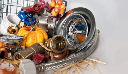 Plumbing fixtures and fall gourds piled in a sink, with brass, chrome, and orange accents.