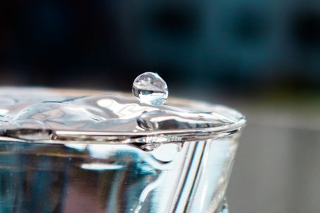 A water droplet suspended above the rim of a clear glass, reflecting light.
