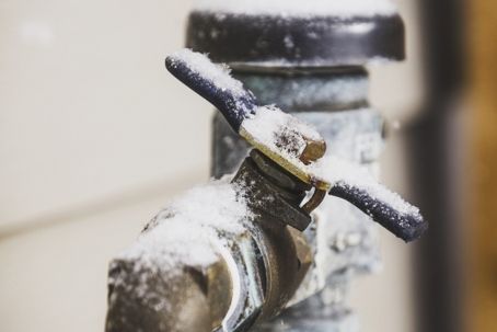 Snow-covered outdoor water faucet; close-up.