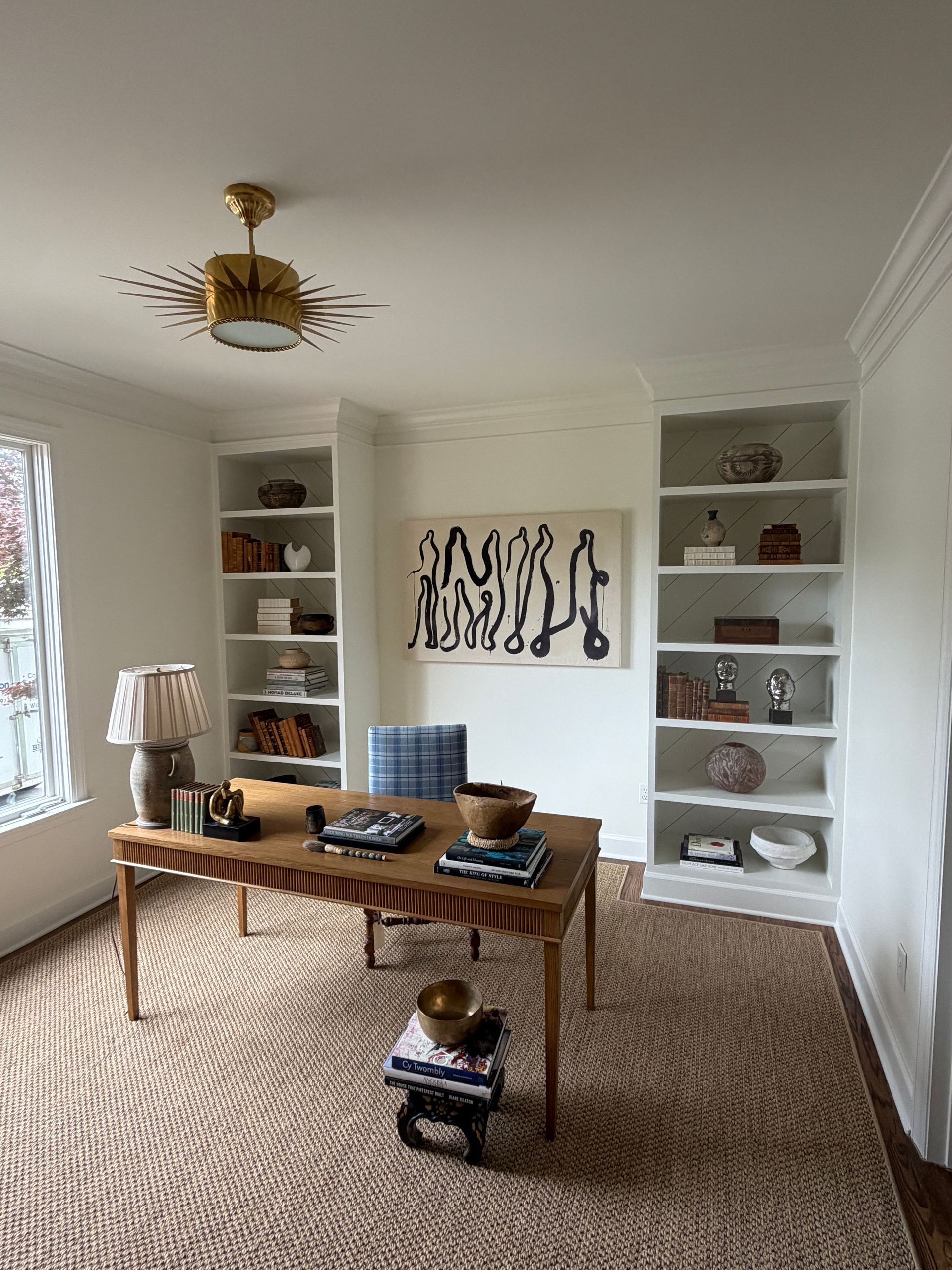 Bright living room with built-in shelves, woven rug, wooden table, and abstract wall art.