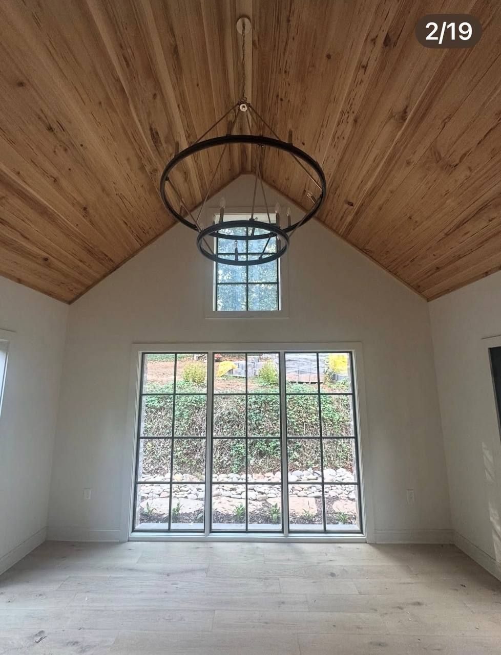 Empty room with high wood ceiling, white walls, large glass doors, and a hanging chandelier.