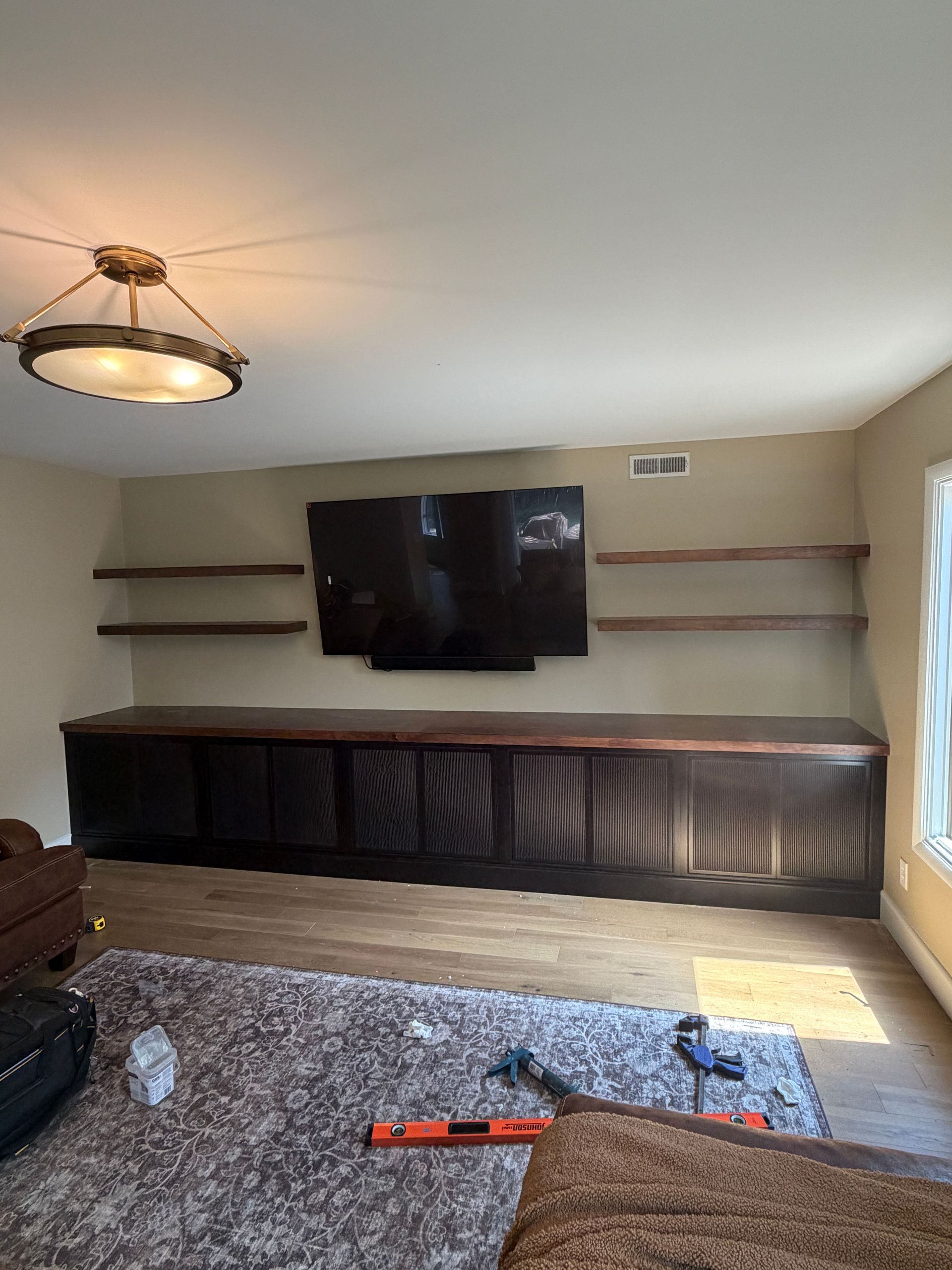 Living room with wall-mounted TV, long cabinet, shelves, ceiling light, and large rug