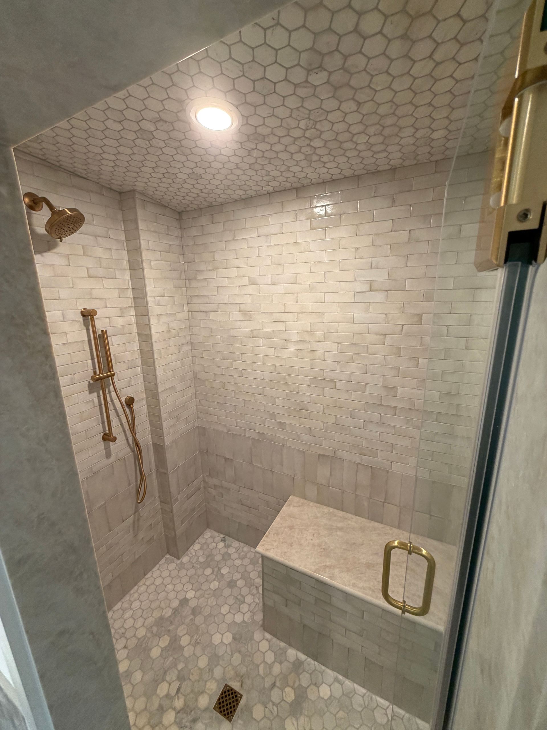 Modern tiled walk-in shower with built-in bench and gold fixtures, viewed from the doorway