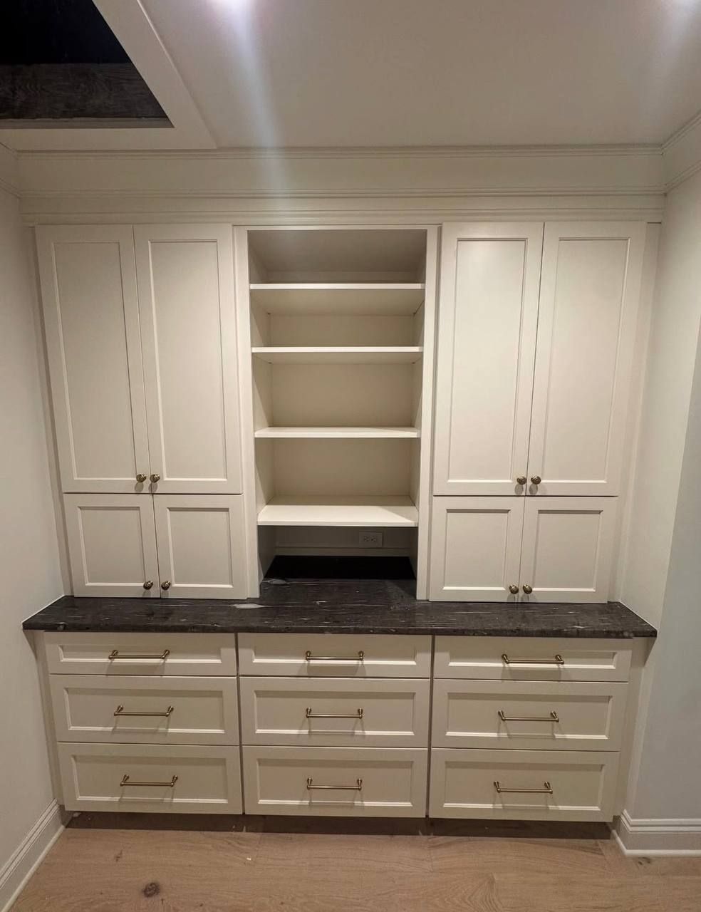 Built-in white cabinets with dark countertop and open shelves in a bright room