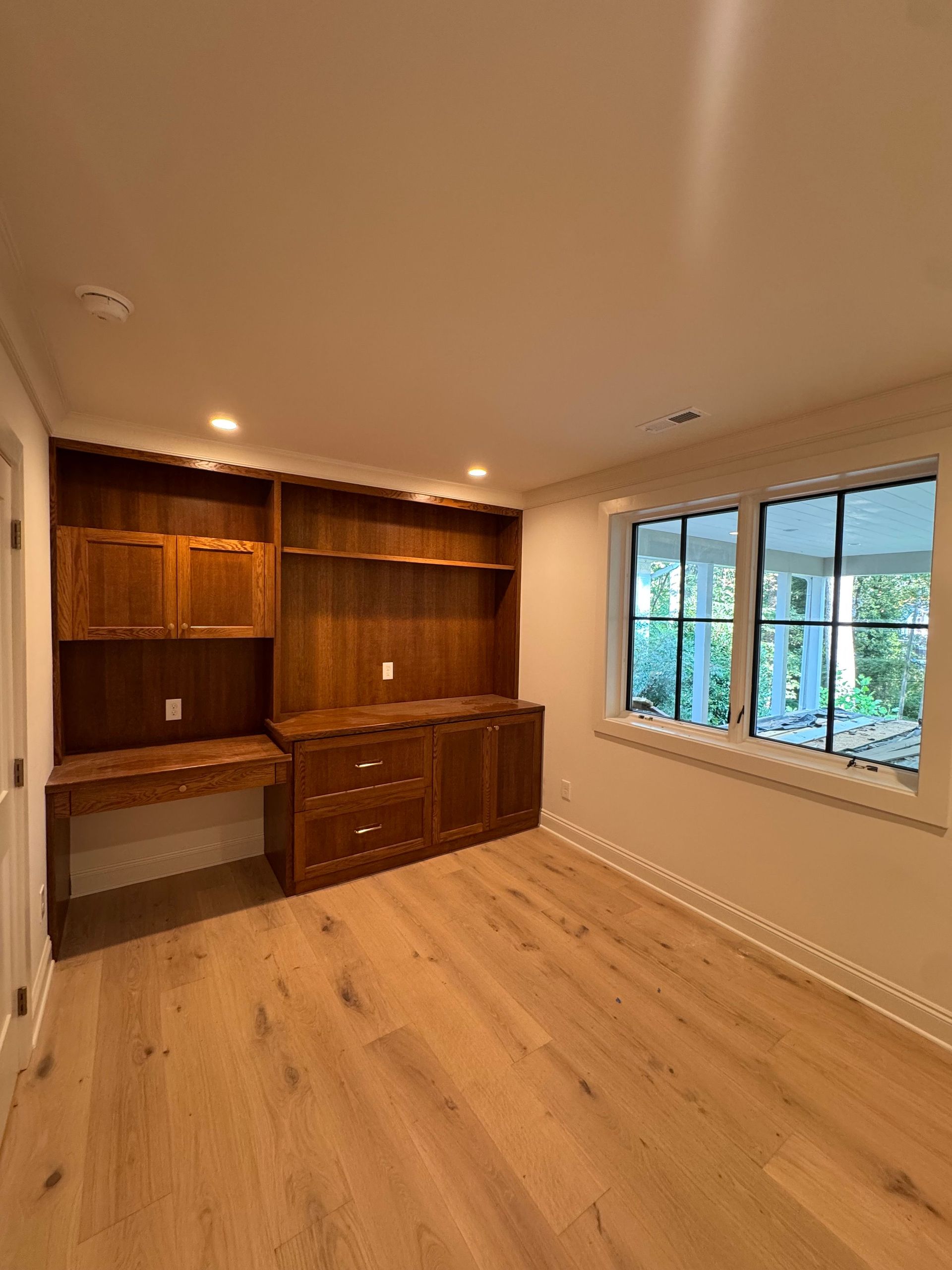 Empty built-in wooden desk and cabinets in a bright room with a window and light wood floor