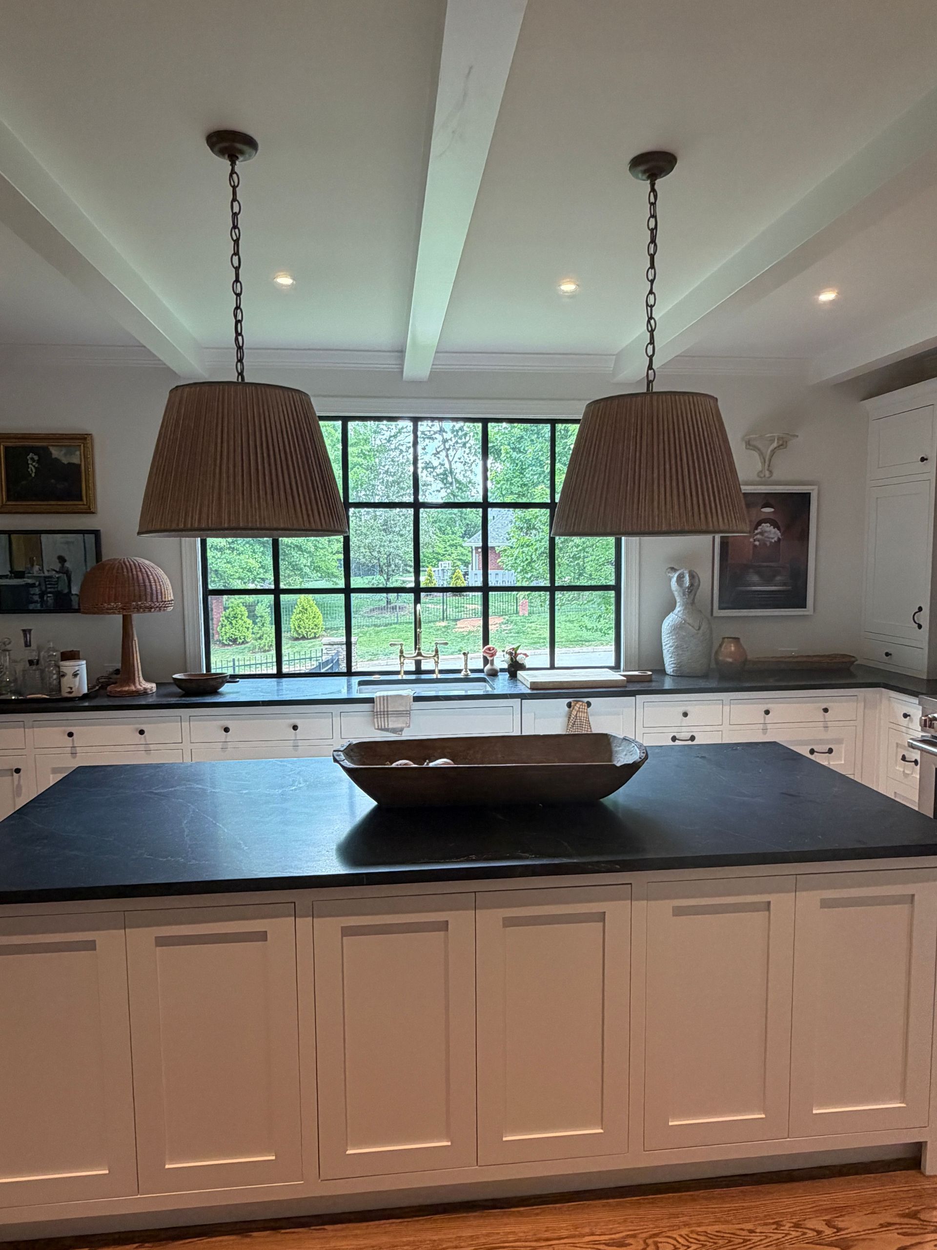Bright kitchen with large window, two hanging pendant lights, and a dark island with a wooden bowl.