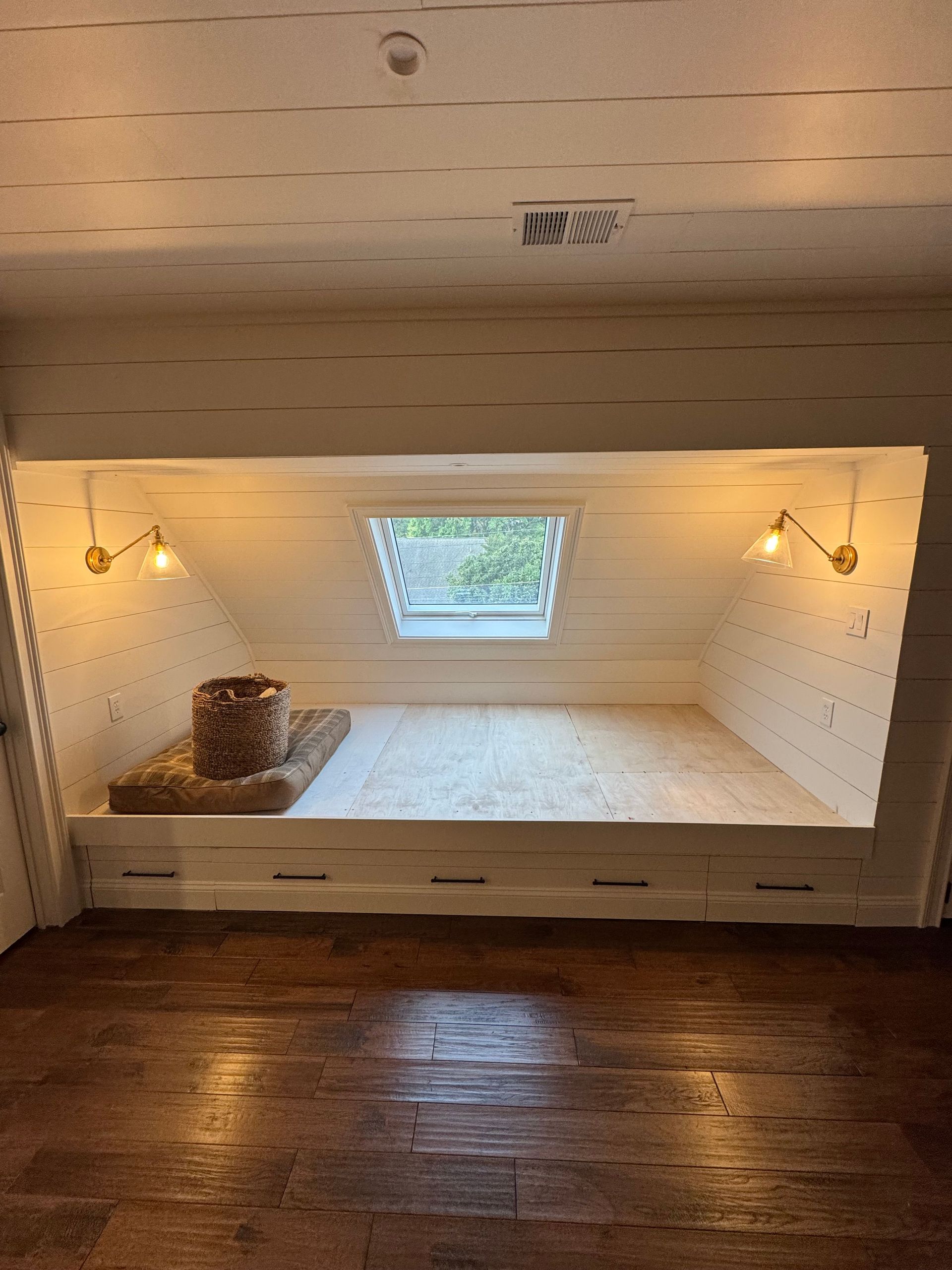 White loft-style nook with built-in platform, warm wall lights, and a small center window.