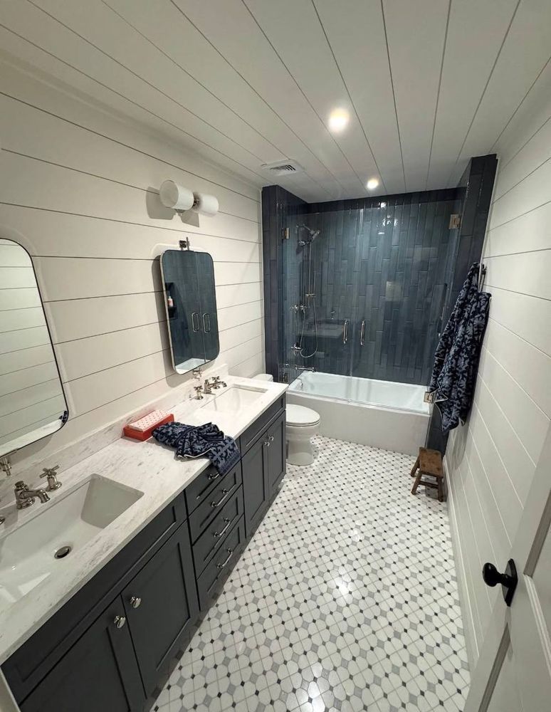 Narrow white bathroom with dark vanity, tub at back, patterned tile floor, and black shower curtain on right.