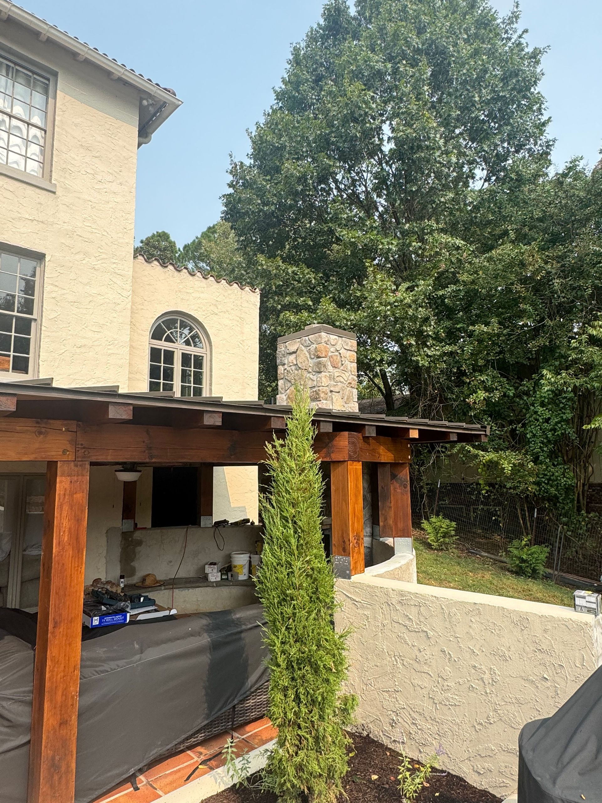 Stone house patio with pergola, tall tree, and a narrow evergreen in the foreground