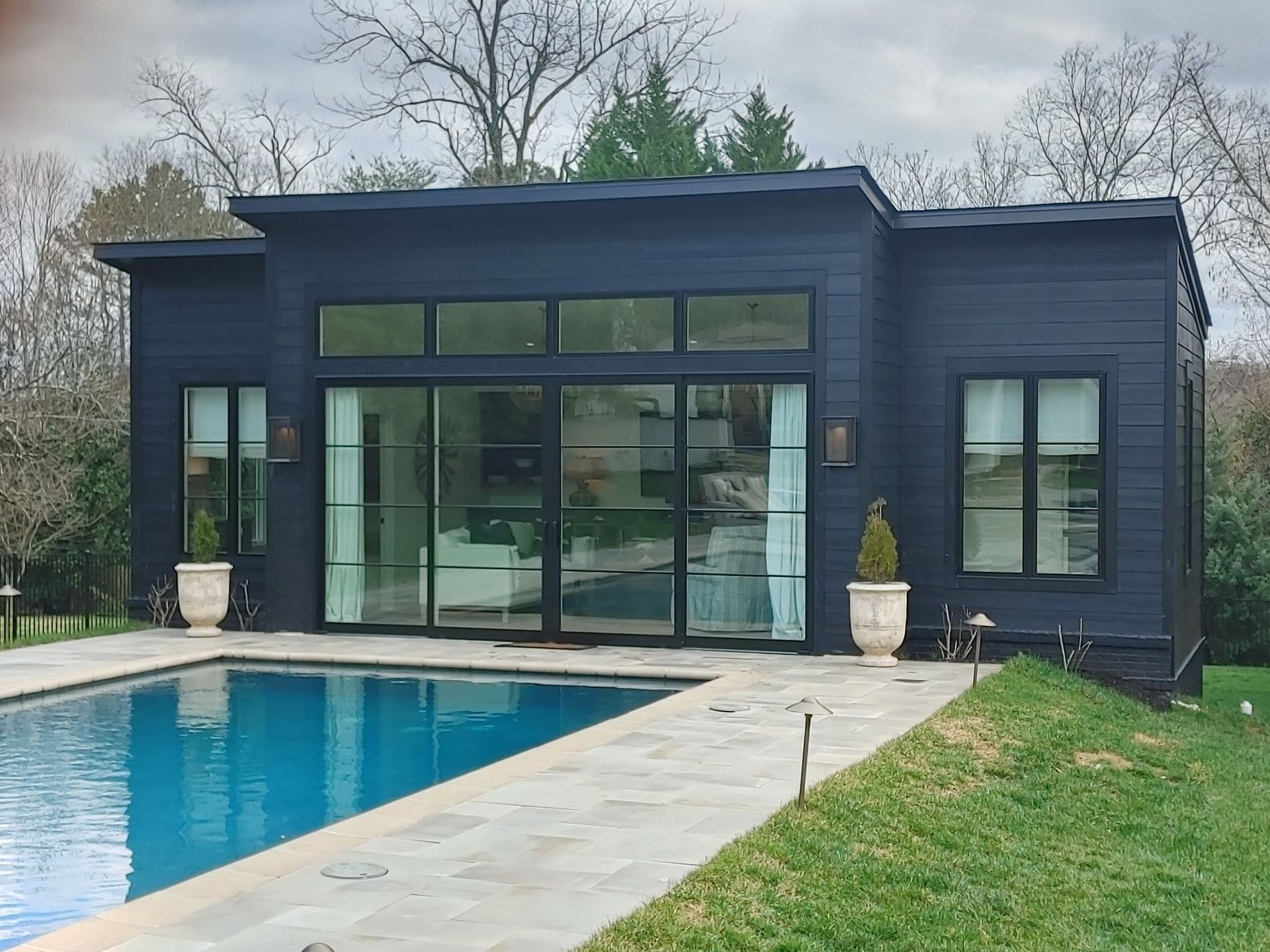 Modern dark-blue pool house with large glass doors beside a backyard swimming pool