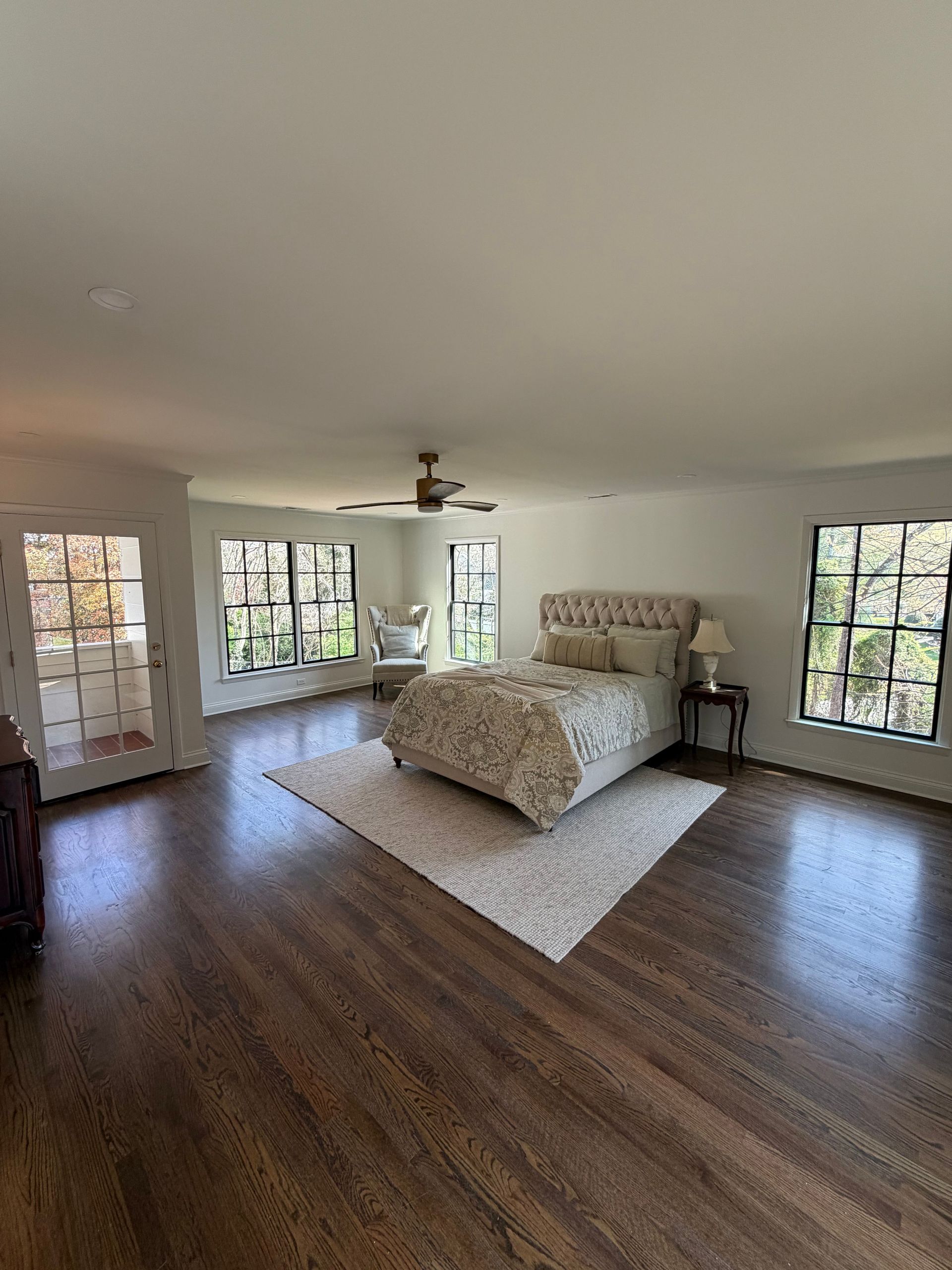 Spacious bedroom with a bed, windows, dark wood floors, and light walls.