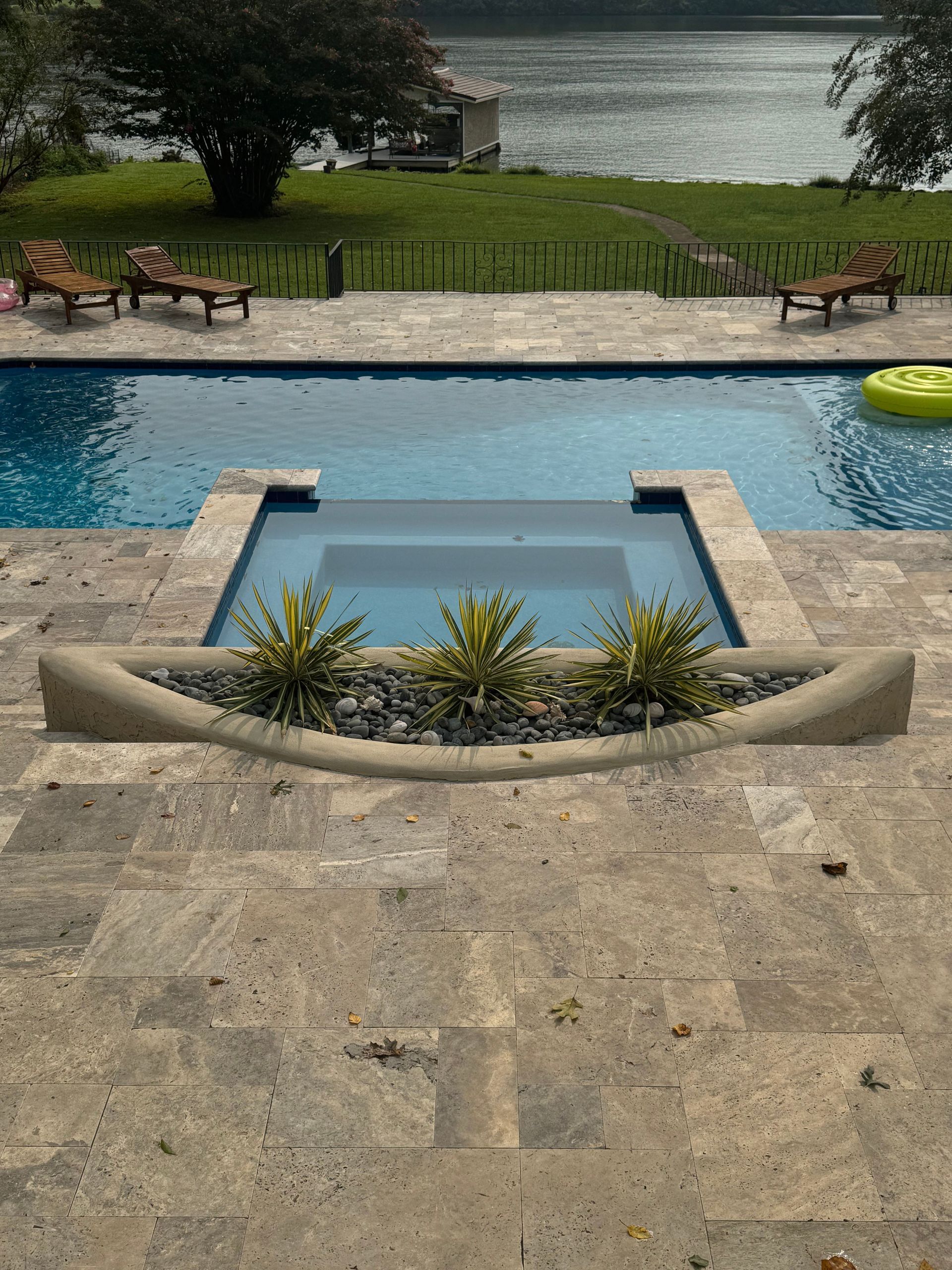 Poolside patio with a small square fountain and lake view beyond a grassy lawn